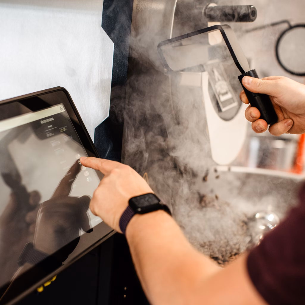 Close-Up-Foto: Person stellt Parameter für den Röstvorgang der Kaffeebohnen ein, Rauch der Röstung im Hintergrund