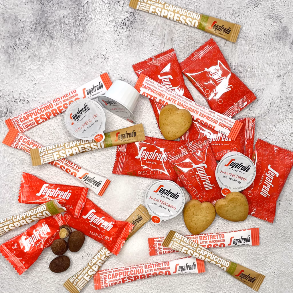 Imagebild Zusatzprodukte mit Zuckersticks, Portionssahne, Schokoladenmandeln und Keksen in Herzform, zum Teil ausgepackt